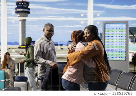 Emotional airport farewell with parents saying goodbye to teen daughter, child leaving to study abroad at university. Young traveler with luggage and passport prepares to airplane alone. Emotional airport farewell with parents saying goodbye to teen daughter, child leaving to study abroad at university. Young traveler with luggage and passport prepares to airplane alone. 138539763