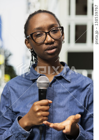 Street interviewer using mic to question pedestrians in city metropolitan area. African american woman working for local television station conducting public opinion poll in town square Street interviewer using mic to question pedestrians in city metropolitan area. African american woman working for local television station conducting public opinion poll in town square 138539767