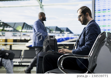 Man entrepreneur preparing for business trip in busy airport terminal lounge, ready for boarding plane and flight departure. Business traveler frequent flyer with tablet and luggage. Man entrepreneur preparing for business trip in busy airport terminal lounge, ready for boarding plane and flight departure. Business traveler frequent flyer with tablet and luggage. 138539771