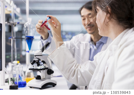 Medical research facility coworkers analyzing sanguine fluid specimen in vial flask, working on disease immunity. Microbiology lab colleagues doing brainstorming, looking at blood samples in test tube 138539843