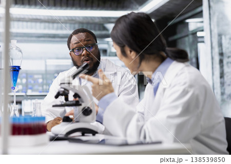 Diverse team of microscopists doing brainstorming in laboratory, inspecting specimen slide for microscopy study. Teamworking lab colleagues reviewing cytology slide for clinical testing procedure Diverse team of microscopists doing brainstorming in laboratory, inspecting specimen slide for microscopy study. Teamworking lab colleagues reviewing cytology slide for clinical testing procedure 138539850