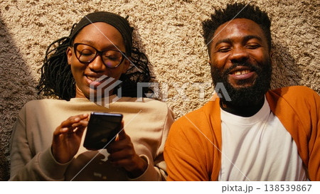 Top down view of black couple laying on the floor and enjoying free time, positive ambience with relaxation and laughter. Two people spending quality time together, serene domestic life. 138539867