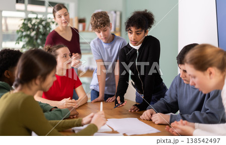 Group of teenagers and students discuss the task at the table in classroom 138542497