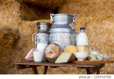 Composition of milk churns and wheels of cheeses on table 138542768
