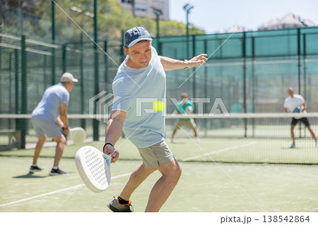 Padel game - man with partners plays on court 138542864