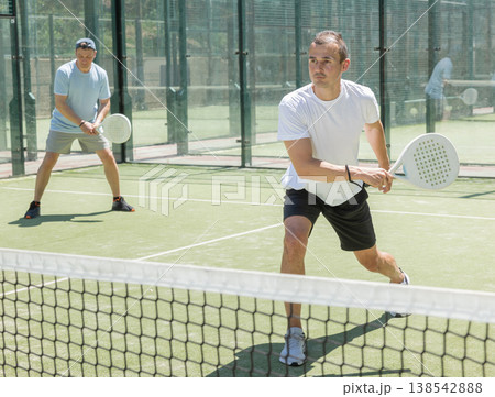Young and adult men playing doubles padel Young and adult men playing doubles padel 138542888