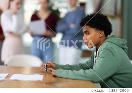 Upset young male student sitting alone at desk Upset young male student sitting alone at desk 138542909
