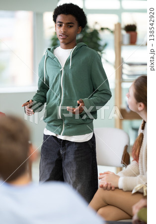 Teenage boy talking to students sitting in circle while teacher watching Teenage boy talking to students sitting in circle while teacher watching 138542920