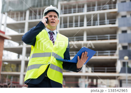 Young engineer, controlling the progress of work on a laptop, talking on a mobile phone Young engineer, controlling the progress of work on a laptop, talking on a mobile phone 138542965