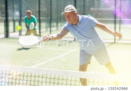 Portrait of sporty mature man playing padel on open court on autumn day, ready to hit ball. Health and active lifestyle concept Portrait of sporty mature man playing padel on open court on autumn day, ready to hit ball. Health and active lifestyle concept 138542966