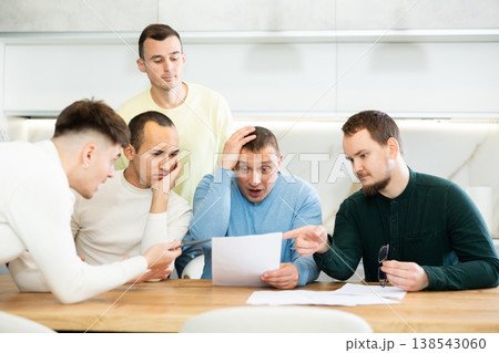 Friends reading financial documents and trying to solve problems together while sitting at table in their kitchen Friends reading financial documents and trying to solve problems together while sitting at table in their kitchen 138543060