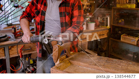 Carpenter equipment. Sanding wood. Man polishing figure piece product with professional electric machine belt sander in joinery workshop. 138544677