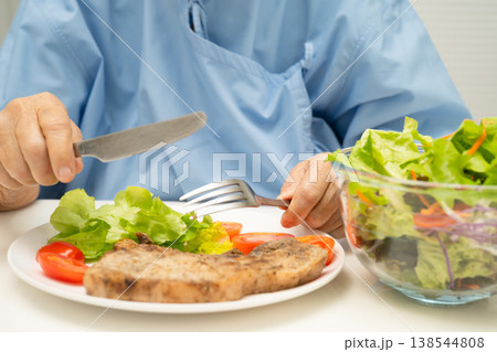 Asian elderly woman patient eating pork chop stake and vegetable salad for healthy food in hospital. Asian elderly woman patient eating pork chop stake and vegetable salad for healthy food in hospital. 138544808