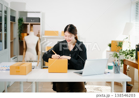 Startup small business SME, Entrepreneur owner woman using smartphone or tablet taking receive and checking online purchase shopping order to preparing pack product box. 138546203