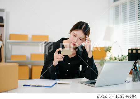 Stressed Asian woman sitting at office desk with parcels and laptop, overwhelmed by online business problems, workload pressure Stressed Asian woman sitting at office desk with parcels and laptop, overwhelmed by online business problems, workload pressure 138546304