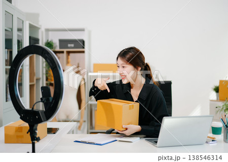 Beautiful Asian lady blogger showing clothes in front of the camera to recording vlog video live streaming at her shop. Online Shopping Cart notion. Beautiful Asian lady blogger showing clothes in front of the camera to recording vlog video live streaming at her shop. Online Shopping Cart notion. 138546314