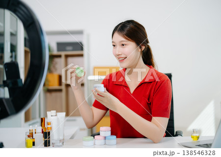 Asian beauty influencer filming skincare review with ring light, showcasing cosmetic jars and products for online content, beauty marketing, and social media promotions. 138546328