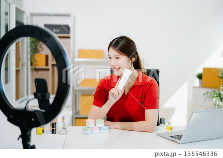 Asian beauty influencer filming skincare review with ring light, showcasing cosmetic jars and products for online content, beauty marketing, and social media promotions. 138546336