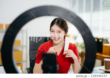 Asian beauty influencer filming skincare review with ring light, showcasing cosmetic jars and products for online content, beauty marketing, and social media promotions. 138546337