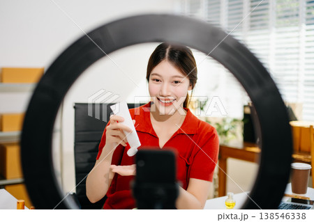 Asian beauty influencer reviewing skincare product on camera with ring light and smartphone for social media marketing, reflecting modern lifestyle 138546338