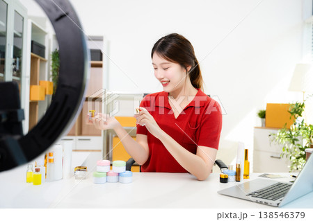 Smiling Asian woman influencer holding cream jar and live streaming for online business in her home office studio Smiling Asian woman influencer holding cream jar and live streaming for online business in her home office studio 138546379