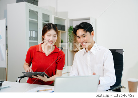 Two Asian coworkers collaborating on business planning, discussing documents and using digital devices in modern office Two Asian coworkers collaborating on business planning, discussing documents and using digital devices in modern office 138546458