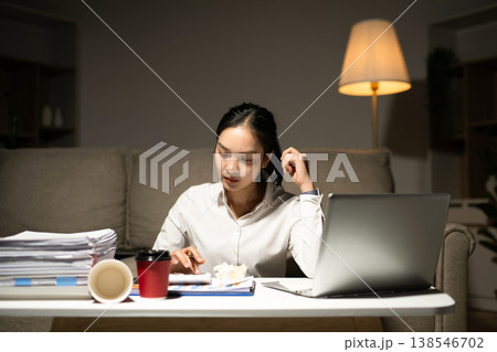 Stressed businesswoman working late at home with laptop and paperwork. Deadline pressure, overtime, workload, finance and modern business lifestyle concept. Stressed businesswoman working late at home with laptop and paperwork. Deadline pressure, overtime, workload, finance and modern business lifestyle concept. 138546702
