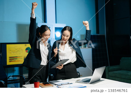 Two businesswomen celebrating success after achieving goals at office desk. Teamwork, motivation, leadership, startup growth and modern corporate workplace. 138546761