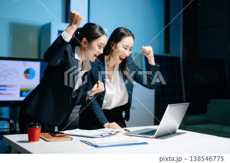 Two businesswomen celebrating success after achieving goals at office desk. Teamwork, motivation, leadership, startup growth and modern corporate workplace. Two businesswomen celebrating success after achieving goals at office desk. Teamwork, motivation, leadership, startup growth and modern corporate workplace. 138546775