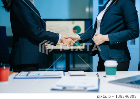 Two businesswomen shaking hands in modern office after agreement. Professional partnership, corporate teamwork, trust, negotiation, success and business collaboration. 138546805