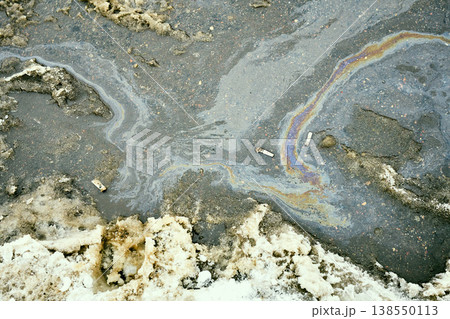 Iridescent oil slick pooling on melting snow and asphalt with cigarette butts, visualizing environmental pollution and urban decay Iridescent oil slick pooling on melting snow and asphalt with cigarette butts, visualizing environmental pollution and urban decay 138550113