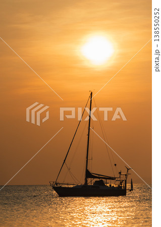 Sailing yacht silhouette anchored on calm sea at golden sunset with bright sun above horizon and shimmering water reflections Sailing yacht silhouette anchored on calm sea at golden sunset with bright sun above horizon and shimmering water reflections 138550252