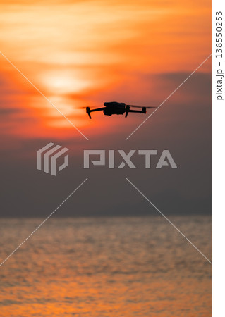 Drone flying over sea at sunset with dramatic sky, concept of unmanned aerial vehicle Drone flying over sea at sunset with dramatic sky, concept of unmanned aerial vehicle 138550253