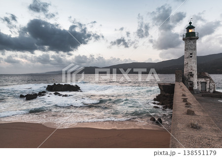 A sturdy stone breakwater supports a classic lighthouse tower. Corsican landscape 138551179