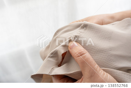 Woman darning a beige clothes by hand with needle and patch fabric 138552768