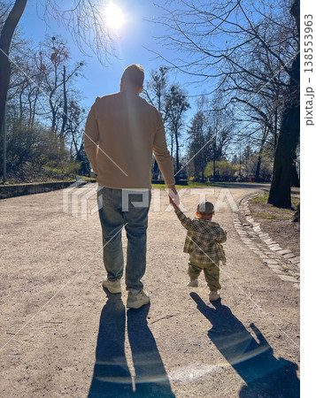 Father holding toddler hand on sunny park path Father holding toddler hand on sunny park path 138553963