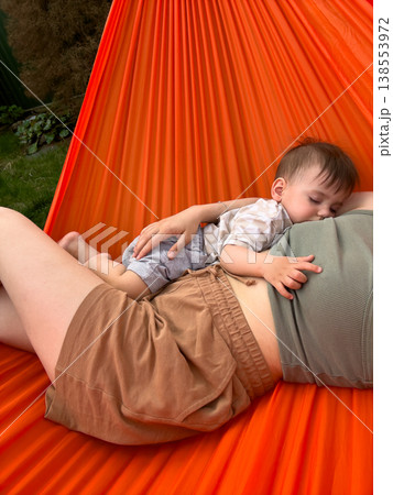 Mother and baby cuddling in orange hammock outdoors Mother and baby cuddling in orange hammock outdoors 138553972