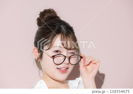 ピンク背景で眼鏡（サングラス）が似合うお団子ヘアのかわいい美人な美容やウィンクのビューティーイメージ 138554675