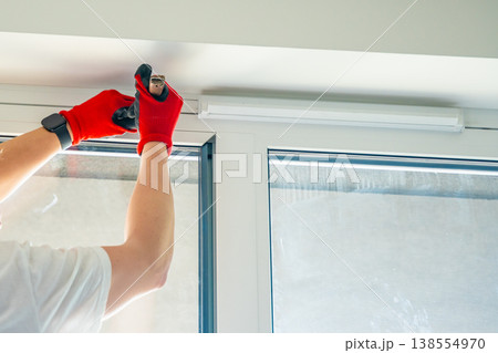 Worker removing window glazing bead from plastic frame during glass replacement in apartment. Home repair and window maintenance process concept. 138554970