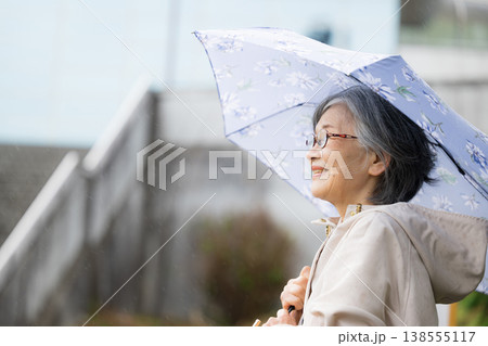 傘をさして梅雨や雨を楽しむ散歩する高齢女性の穏やかで健康的な見上げるアクティブシニアクローズアップ	 138555117