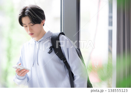 真顔でスマートフォンを見る大学生の若い男性の日常と通学シーン 真顔でスマートフォンを見る大学生の若い男性の日常と通学シーン 138555123