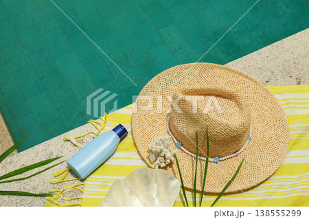 A sun hat and sunscreen are on a towel near the pool A sun hat and sunscreen are on a towel near the pool 138555299