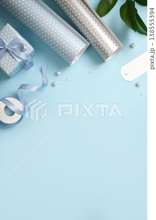 Gift wrapping with blue and silver wrapping paper, ribbon, scissors, and small gift boxes on blue backdrop. Copy space. Gift wrapping with blue and silver wrapping paper, ribbon, scissors, and small gift boxes on blue backdrop. Copy space. 138555394