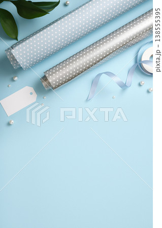 Gift wrapping background. Paper rolls, gift tag, and pearls on blue desk. Copy space for holiday text or design. Gift wrapping background. Paper rolls, gift tag, and pearls on blue desk. Copy space for holiday text or design. 138555395