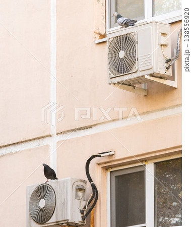 air conditioner is installed on facade of the building. air conditioner compressor is on wall. 138556920