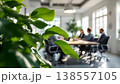 Photo of business meeting in modern office with green plant in foreground, showcasing collaboration and corporate environment. 138557105