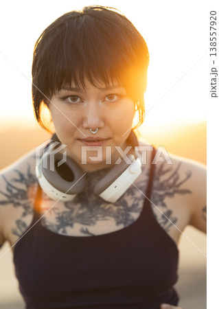 Young woman with headphones and tattoos standing outdoors Young woman with headphones and tattoos standing outdoors 138557920