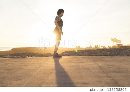 Woman exercising on beach path during golden sunset 138558265