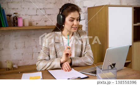 Young woman in headphones studying online with laptop at home desk. 138558396