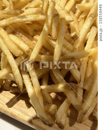 Close up of crispy french fries on wooden plate. Concept of fast food, snack, and unhealthy eating. Golden fried potatoes with crunchy texture and appetizing look. Close up of crispy french fries on wooden plate. Concept of fast food, snack, and unhealthy eating. Golden fried potatoes with crunchy texture and appetizing look. 138558449